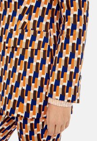 Musteranzug mit rechteckigen Formen in Blau, Orange, Braun und Beige. Enthält eine Tasche und ein strukturiertes Manschettendetail.