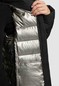 Black puffer jacket with a shiny silver insulated lining. Features a quilted design and front opening, revealing a side pocket within the lining.