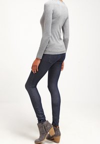 Sudadera gris de manga larga, jeans ajustados azul oscuro y botas gris con tacón de madera apilado y detalle de borlas.