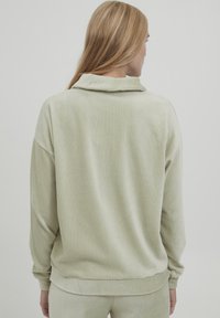 Ljusgrön velourtröja med vikbar krage, ribbad textur, nedhasade axlar och muddade ärmar. Avslappnad passform, mjuk yta.