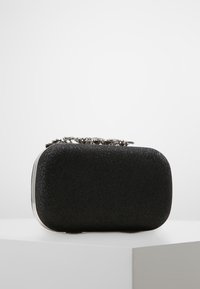 Liten svart rektangulär kuvertväska med en glittrig textur och en utsmyckad silverfärgad dekorativ spänne upptill.