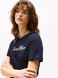 T-shirt en coton bleu marine avec un logo "Tommy Hilfiger" brodé en blanc sur la poitrine, accompagné d'un petit logo rouge, blanc et bleu sur la manche.