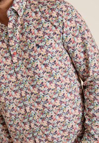 Bloemenpatroon shirt in lichtroze met blauwe, rode en groene accenten. Voorzien van knopen, een kraag en een relaxte pasvorm. Katoenen stoftextuur.