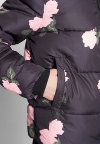 Černá prošívaná bunda s velkými růžovými růžovými vzory, žebrovanými manžetami a boční kapsou, z hladkého, lesklého materiálu.