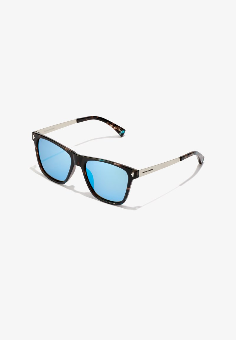Ruudukujulised tarsustel päikeseprillid siniste peegelobjektiividega ja hõbedast metallkätkedega, millel on silt "HAWKERS", valgel taustal.