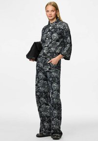 Set od crnog denima s cvjetnim uzorkom, koji uključuje jaknu s ovratnikom, dugmadi i slobodnim širokim nogavicama. Teksturirana tkanina.