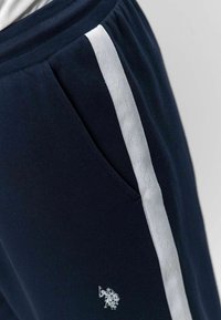 Pantalon de survêtement bleu marine en mélange de coton, avec une bande logo verticale blanche et une poche latérale. Détail logo brodé sur le devant.