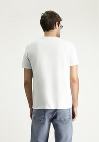 T-shirt bianca a maniche corte con una superficie liscia, scollatura rotonda e una vestibilità comoda, abbinata a jeans in denim azzurro chiaro.