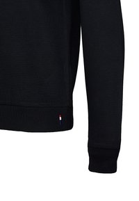 Czarny sweter z prążkowanymi mankietami i dołem, wykonany z gładkiego materiału. Posiada małe logo w trzech kolorach blisko dołu.