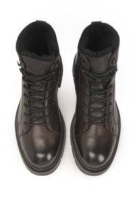 Botas de cuero marrón con cordones, suela gruesa, forro negro aterciopelado y cuello acolchado. Presenta ojales de metal y una textura suave.