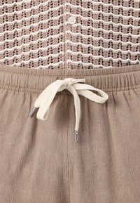 Light brown pants with a textured surface, elastic waistband, and cream drawstring. Top features a patterned knit design with buttons.