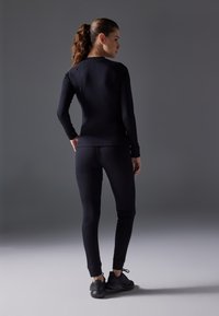Haut noir à manches longues et leggings en tissu extensible, présentant une coupe ajustée, des poignets côtelés et des chaussures de sport noires assorties.