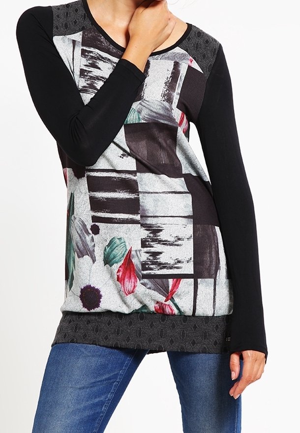 Femme portant un haut à manches longues avec des manches noires et un motif abstrait à l'avant comportant des fleurs et des formes géométriques, assorti à un jean bleu.