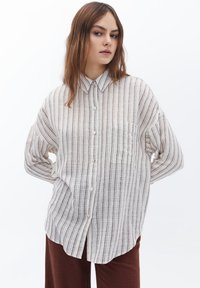 Camicia button-up in beige chiaro con righe verticali marroni, vestibilità rilassata, colletto a punta e taschino sul petto; tessuto leggero.