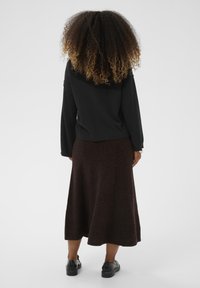 Crna majica s dugim rukavima, uparena s smešnom, do koljena, teksturiranom suknjom. Crna obuća upotpunjuje odjevnu kombinaciju.