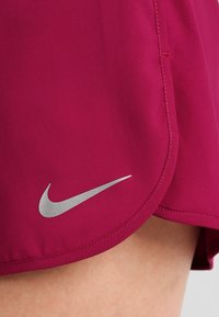 Pantalones cortos deportivos de color magenta, fabricados con tela suave y ligera. Presentan un logo plateado de Nike en la parte inferior izquierda y un dobladillo curvado.