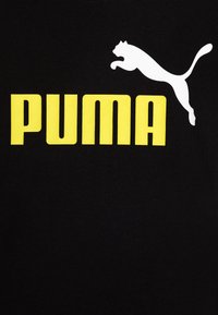 Camiseta de algodón negra con un destacado logo amarillo de "PUMA" y una silueta blanca de un puma saltando. Textura suave, diseño casual.