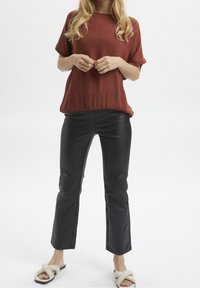 Haut rouille à manches courtes en tissu texturé ; pantalon en cuir noir ; sandales à glisser crème avec un détail en nœud.