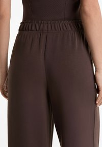 Braune, elastische Hosen mit glatter Textur. Sie verfügen über einen taillierten oberen Teil und weite, fließende Beine, die ein einfaches Design zeigen.