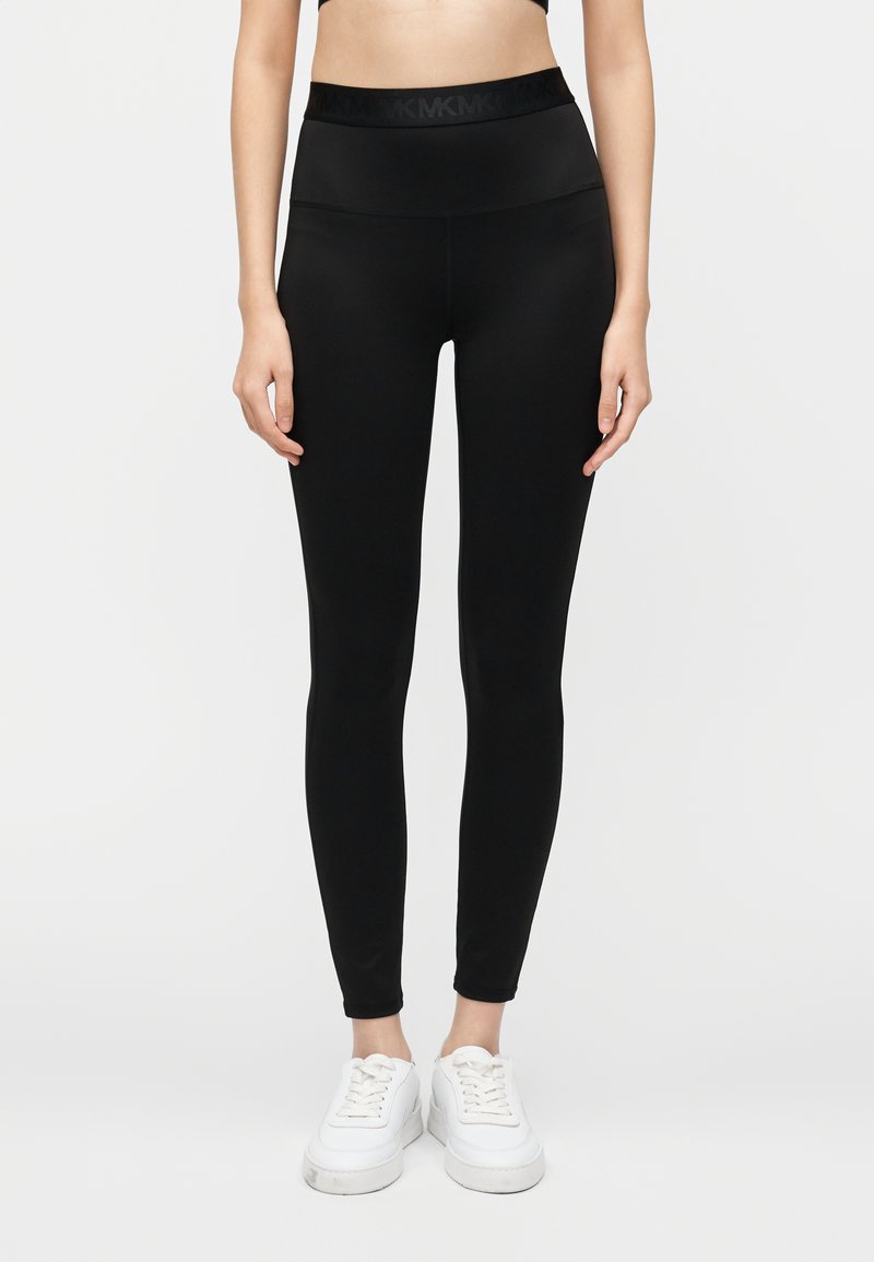 Mustat, korkeavyötäröiset leggingsit joustavasta materiaalista, jossa on sileä pinta. Niissä on leveä, vartaloa myötäilevä vyötärönauha. Yhdistetty valkoisiin tennareihin.