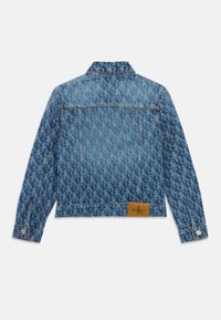 Chaqueta de mezclilla en azul claro con un patrón de logotipos repetido, puños abotonados y un parche de cuero con el logo en la parte baja de la espalda.