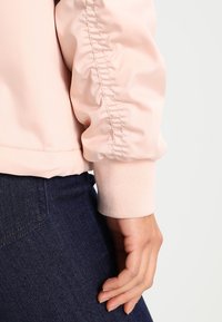 La giacca bomber rosa chiaro presenta un tessuto morbido con polsini a costine, design delle maniche arricciate e una vestibilità rilassata. Abbina a denim scuro.