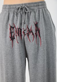 Grå joggebukser med elastisk midje og snor, med svart og rødt grafisk tekstdesign foran i en brennende stil.