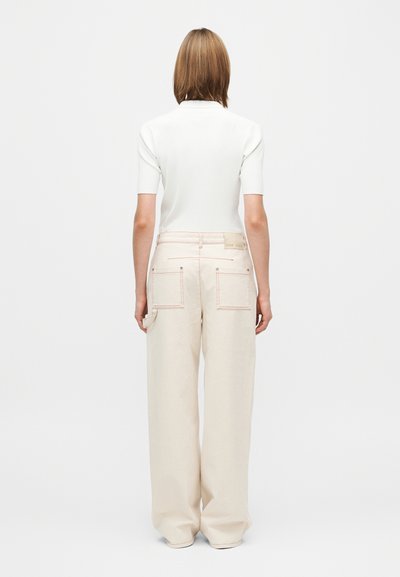 Valkoinen, ribbineuloksinen lyhythihainen paita yhdistettynä leveälahkeisiin beigeihin housuihin, joissa takataskut ja hienovarainen kontrastipistely.