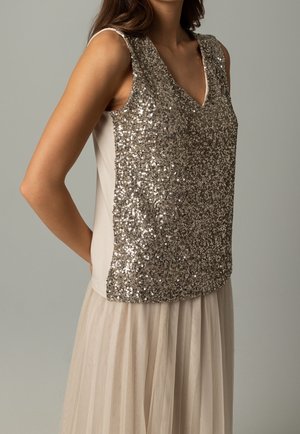 Top de tirantes con lentejuelas, cuello en V en tonos dorado y beige. La parte delantera del top es brillante y texturizada, mientras que la parte trasera es lisa y sólida. Tejido ligero.