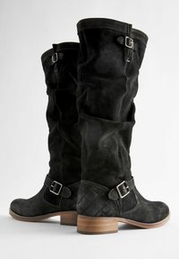 Bottes en suède noires montant jusqu'aux genoux, ornées d'une sangle en cuir texturé et d'une boucle en argent. Talon en bois avec un motif matelassé sur le côté.