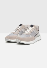Zapatillas de ante y malla en gris claro con cordones blancos. Presenta una suela blanca gruesa y un acento en azul marino en el talón. Material superior texturizado.