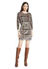 Korte mouwen ruitjesjurk in zwart, wit en bruin, getailleerde silhouet, gecombineerd met kniehoge bruine leren laarzen met spitse neuzen.