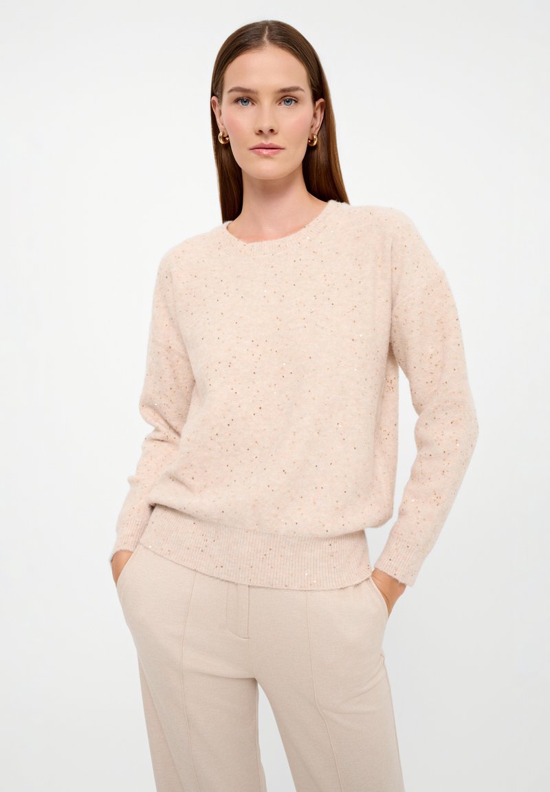 Maglione rosa chiaro con collo rotondo, maniche lunghe e orlo a coste. Presenta sottili macchie distribuite su tutto il tessuto. Texture morbida.
