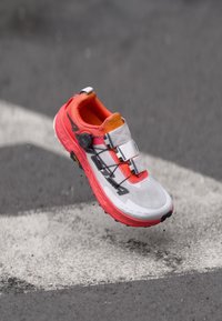 Bright red and white running shoe with a textured mesh upper, adjustable lace system, orange accents, and a rugged outsole.