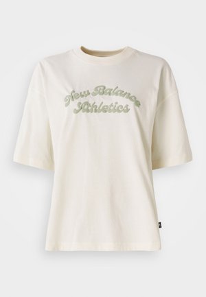 T-shirt en coton crème à manches courtes, avec un graphisme en texte vert incurvé qui indique "New Balance Athletics."