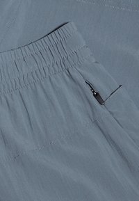 Ljusblå byxor med elastisk midja, som har en ficka på sidan med dragkedja och subtil textur. Slät tyg med sydda detaljer.