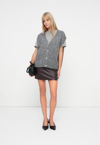 Gray wool cardigan with short sleeves and front buttons, layered over a light gray top, paired with a sleek brown leather skirt and black heels.