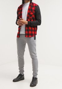 Camicia di flanella a quadretti rossi e neri con maniche nere; t-shirt bianca sotto; pantaloni della tuta grigi; sneaker nere strutturate.