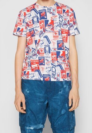 Short-sleeve t-shirt with a cream background, featuring a colorful, repeated graphic print in red and blue, paired with blue tie-dye shorts.