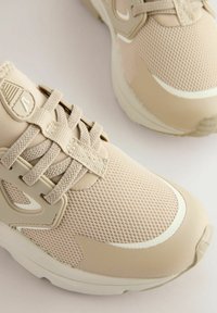 Beige atletiske sko med mesh og syntetisk materiale, rund tå, tekstureret overflade og snørebånd. Udstyret med formede detaljer på siderne.