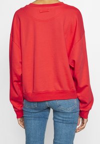 Czerwona, oversize'owa bluza z prążkowanym dołem i mankietami. Posiada szeroki okrągły dekolt i opuszczone szwy na ramionach, wykonana z miękkiej bawełny.