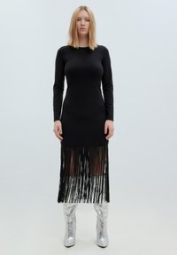 Schwarzes langärmliges Kleid mit Fransen-Saum, aus glattem Stoff. Kombiniert mit glänzenden silbernen kniehohen Stiefeln. Minimalistisches Design, ohne Muster.