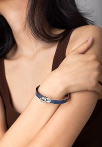 Bracciale rigido blu navy con finitura lucida e un gancio in stile fibbia argentato decorato con piccole pietre trasparenti.