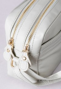 Gray leather bag with two parallel gold zippers, a textured finish, and stitched accents. Features gold hardware and a detachable strap.