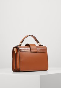 Ruskea nahkalaukku, jossa on jämäkkä muoto, crocodile-kuosisella läpällä, kultaisilla yksityiskohdilla ja lyhyellä kahvalla. Suurimman osan pinnasta sileä, yksinkertaisilla yksityiskohdilla.