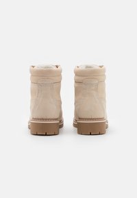 Bottines en suède beige avec une doublure douce et blanche et une semelle en caoutchouc brun épais et texturé. Détails de couture le long des coutures.