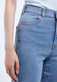 Jeans de mezclilla azul claro con cintura alta, ajuste Slim y acentos de costura sutiles. Presentan bolsillos frontales y un acabado limpio.