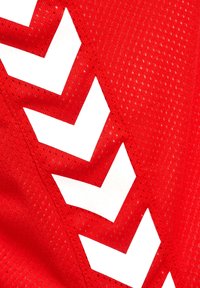 Rotes Netzsportgewebe mit großen weißen Chevron-Mustern, mit einer strukturierten Oberfläche und kleinen Perforationen für Atmungsaktivität.