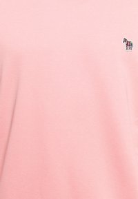 Ljust rosa bomull T-shirt med en liten flerfärgad zebra-broderi på vänster bröstområde. Mjuk textur, avslappnad design.