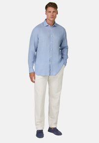 Camicia di lino a maniche lunghe azzurro chiaro con colletto a bottoni, abbinata a pantaloni color crema e scarpe slip-on blu scuro.